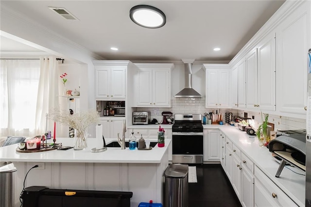 kitchen featuring white cabinets, wall chimney range hood, stainless steel range, a kitchen bar, and decorative backsplash