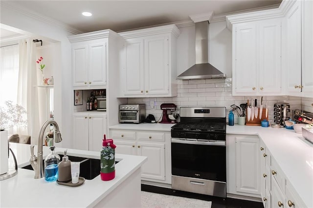 kitchen featuring white cabinets, ornamental molding, wall chimney range hood, stainless steel stove, and decorative backsplash