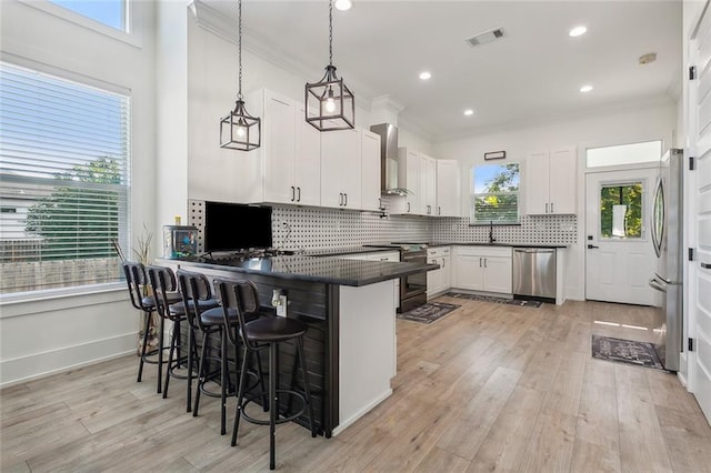 kitchen with white cabinets, decorative light fixtures, wall chimney range hood, and a wealth of natural light