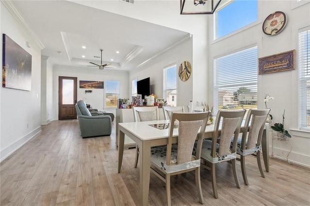 dining room featuring light wood-type flooring, crown molding, a tray ceiling, and ceiling fan