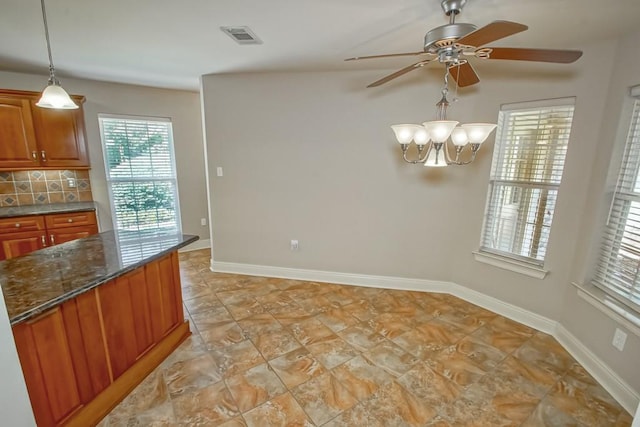 kitchen with decorative backsplash, ceiling fan with notable chandelier, decorative light fixtures, and dark stone counters