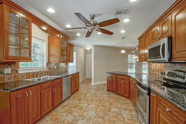 kitchen with sink, backsplash, appliances with stainless steel finishes, dark stone countertops, and ceiling fan