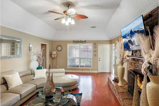 living room featuring a tray ceiling, dark hardwood / wood-style flooring, ceiling fan, and a brick fireplace