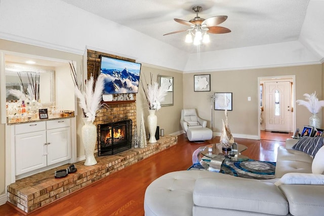 living room featuring wood-type flooring, a tray ceiling, ceiling fan, and a brick fireplace