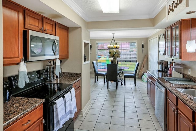 kitchen with light tile patterned flooring, appliances with stainless steel finishes, a notable chandelier, dark stone counters, and crown molding