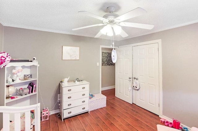 bedroom with wood finished floors, ornamental molding, a closet, baseboards, and a ceiling fan