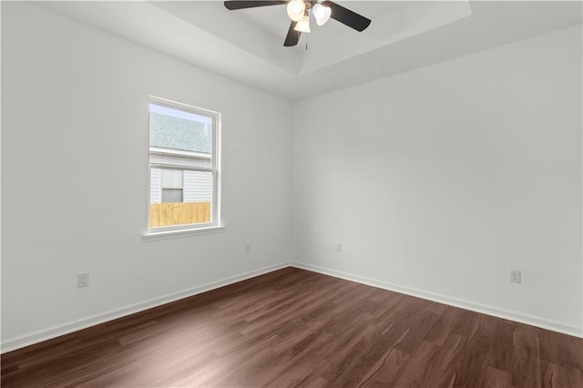 empty room with dark hardwood / wood-style floors, a raised ceiling, and ceiling fan