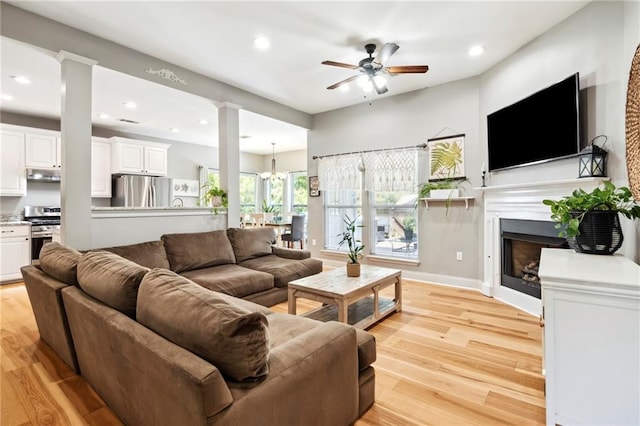 living room featuring ceiling fan with notable chandelier, light wood-type flooring, and ornate columns