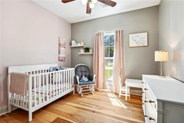 bedroom featuring light wood-type flooring, ceiling fan, and a nursery area