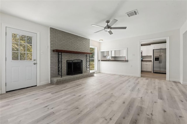 unfurnished living room with visible vents, a ceiling fan, a brick fireplace, light wood-type flooring, and baseboards