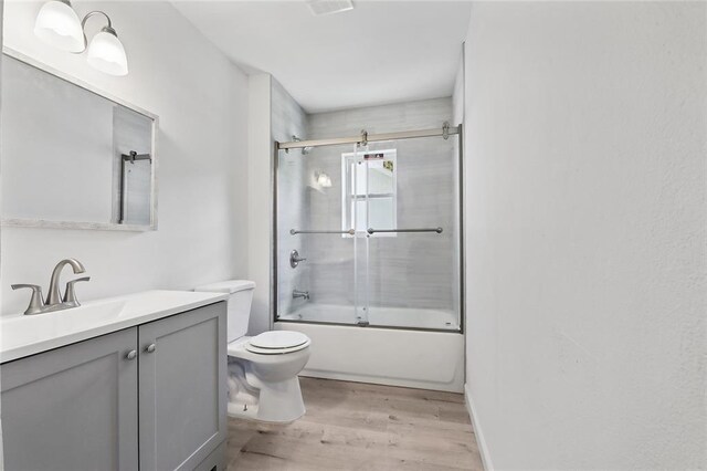 full bathroom with vanity, combined bath / shower with glass door, wood-type flooring, and toilet