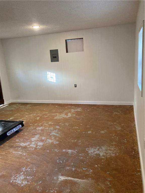 empty room with electric panel, a textured ceiling, and baseboards