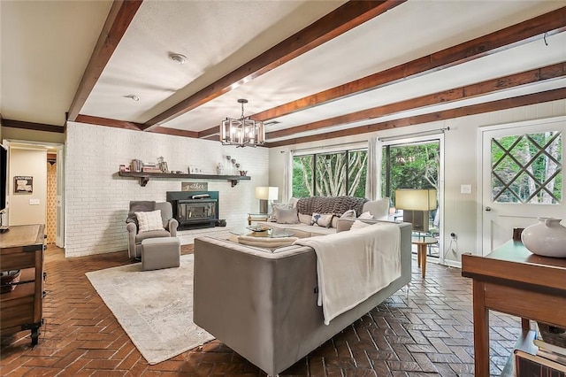 living room featuring an inviting chandelier, a wood stove, beam ceiling, and brick wall