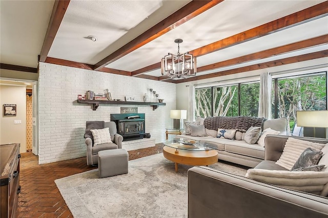 living room featuring beam ceiling, an inviting chandelier, a wood stove, and brick wall