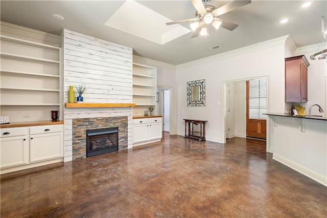 living room featuring a stone fireplace, crown molding, ceiling fan, built in features, and sink