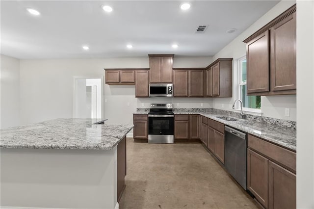 kitchen featuring light stone countertops, dark brown cabinets, appliances with stainless steel finishes, and sink