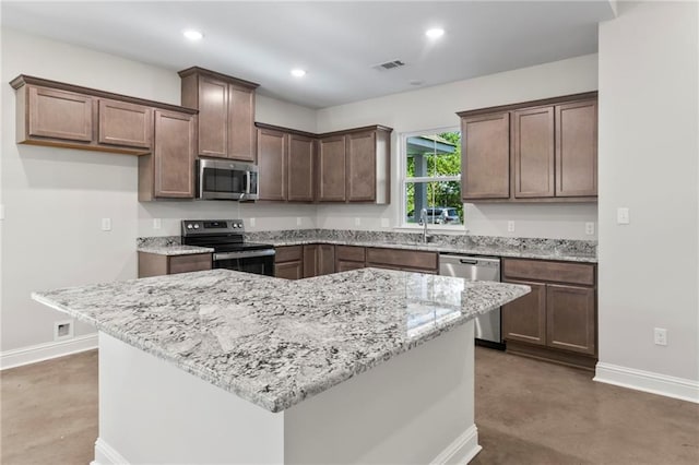 kitchen featuring light stone countertops, stainless steel appliances, concrete flooring, and a center island