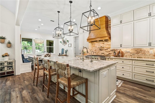 kitchen featuring light stone counters, white cabinets, hanging light fixtures, a kitchen island with sink, and dark hardwood / wood-style flooring