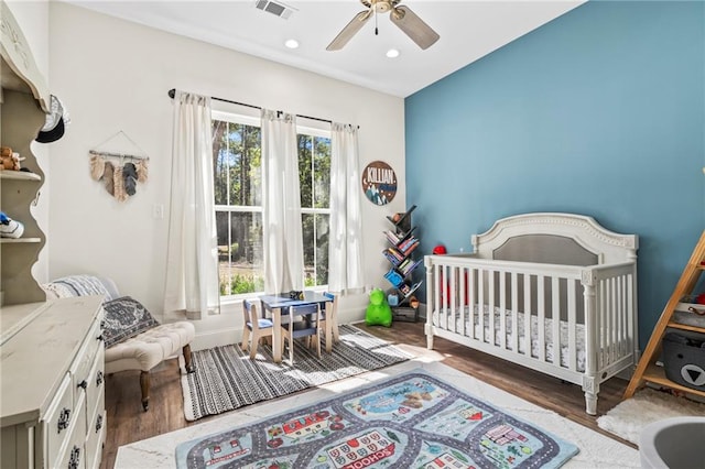 bedroom featuring ceiling fan, a crib, and dark wood-type flooring