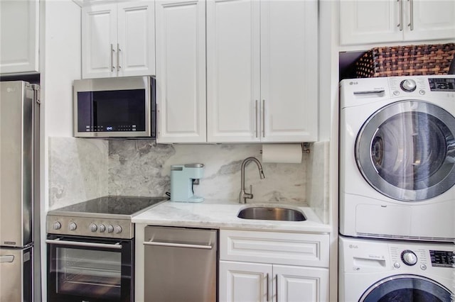 interior space featuring white cabinetry, sink, stainless steel appliances, and stacked washer / dryer