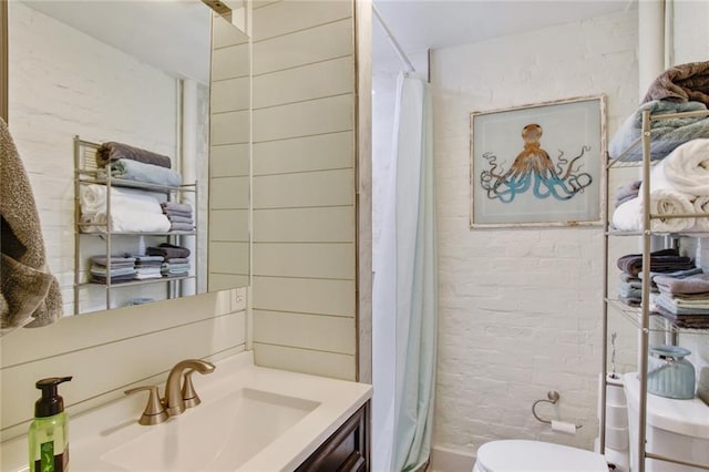 bathroom featuring a shower with curtain, brick wall, toilet, and vanity