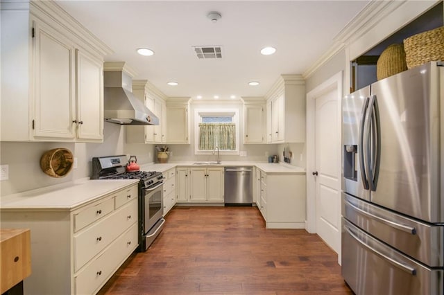 kitchen with appliances with stainless steel finishes, wall chimney exhaust hood, crown molding, cream cabinets, and dark hardwood / wood-style floors