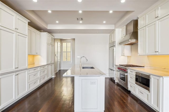 kitchen featuring dark hardwood / wood-style floors, sink, high end appliances, wall chimney exhaust hood, and a center island with sink