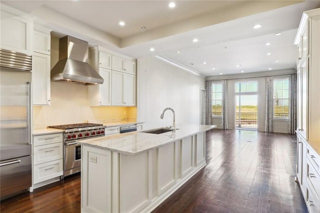 kitchen with an island with sink, wall chimney exhaust hood, premium appliances, dark hardwood / wood-style flooring, and sink