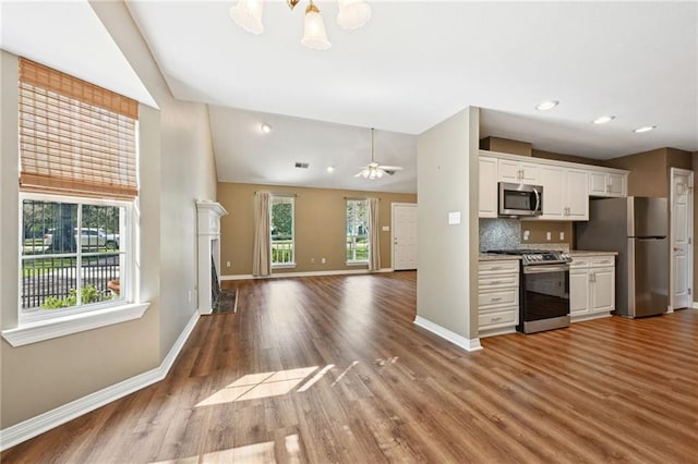 kitchen featuring white cabinetry, vaulted ceiling, decorative backsplash, appliances with stainless steel finishes, and hardwood / wood-style floors