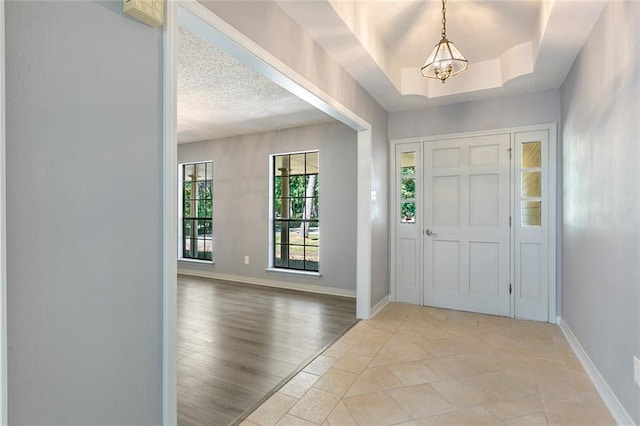 foyer entrance featuring light wood-type flooring, a raised ceiling, and a notable chandelier