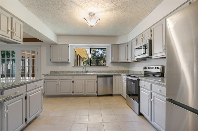 kitchen featuring sink, gray cabinets, light tile patterned floors, light stone counters, and stainless steel appliances