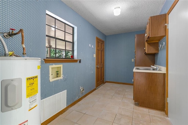 kitchen with electric water heater, sink, light tile patterned floors, and a textured ceiling