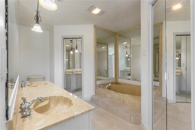 bathroom with tile patterned floors, vanity, a textured ceiling, tiled bath, and toilet