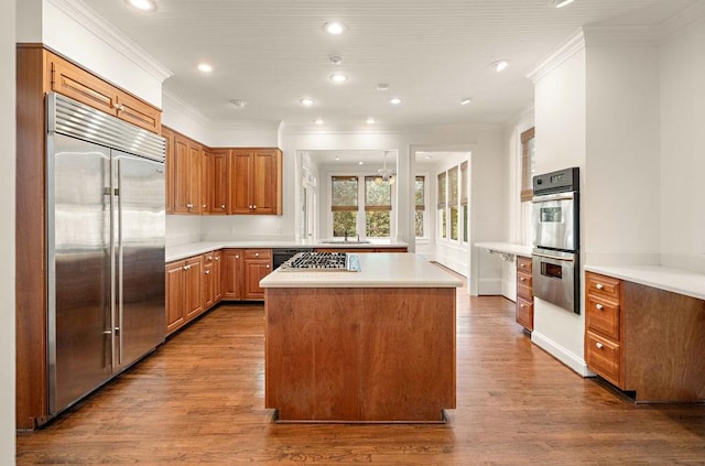 kitchen with crown molding, appliances with stainless steel finishes, a kitchen island, and hardwood / wood-style floors