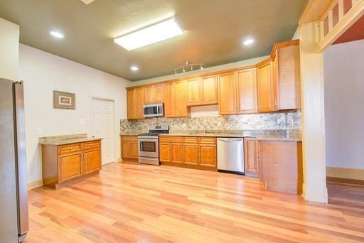 kitchen with light wood-type flooring, appliances with stainless steel finishes, tasteful backsplash, and sink