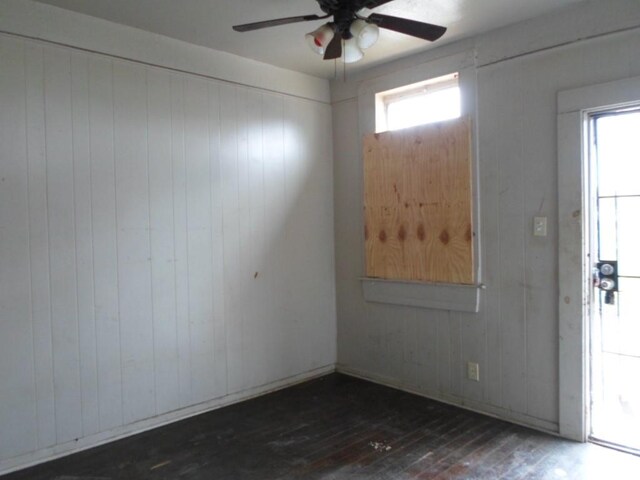 empty room with a wealth of natural light, wood walls, ceiling fan, and dark hardwood / wood-style flooring