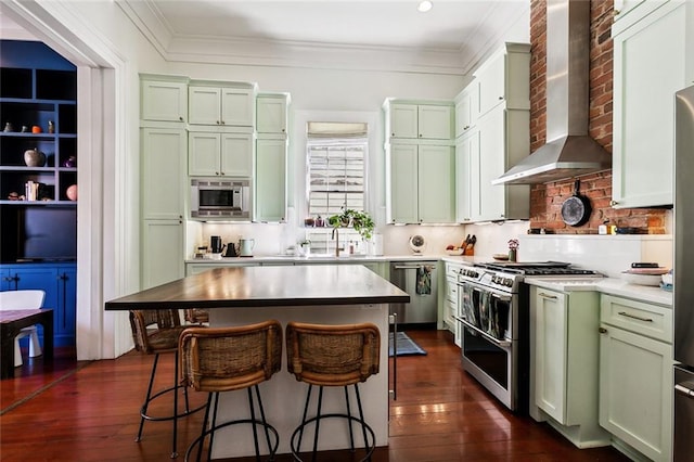 kitchen with green cabinetry, stainless steel appliances, and wall chimney range hood