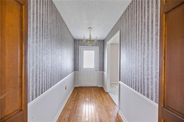 doorway featuring an inviting chandelier, light hardwood / wood-style floors, and a textured ceiling