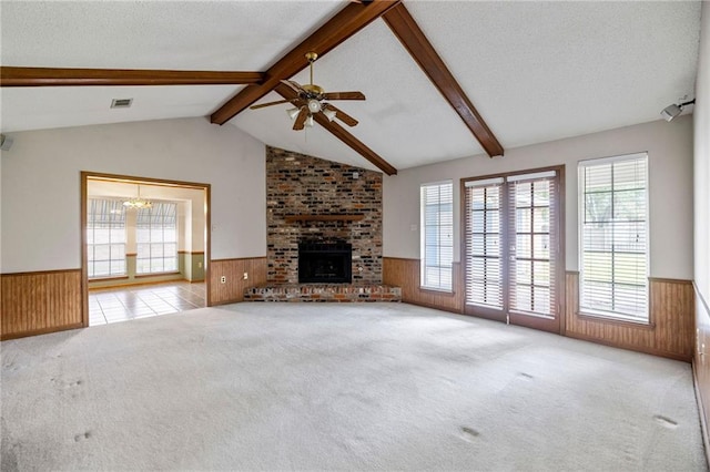 unfurnished living room with wood walls, a textured ceiling, a fireplace, light carpet, and ceiling fan with notable chandelier