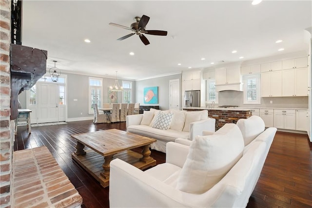 living room with ceiling fan with notable chandelier, crown molding, and dark wood-type flooring