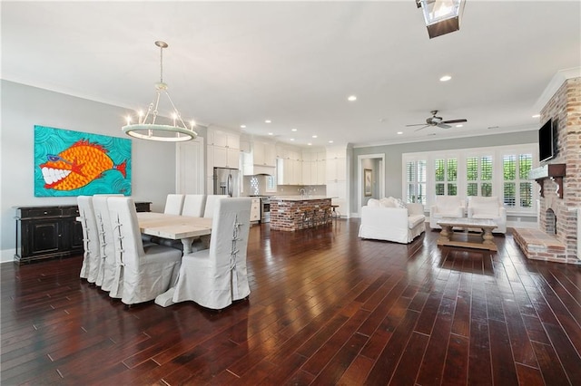 dining space featuring ceiling fan with notable chandelier, ornamental molding, a fireplace, and dark hardwood / wood-style flooring