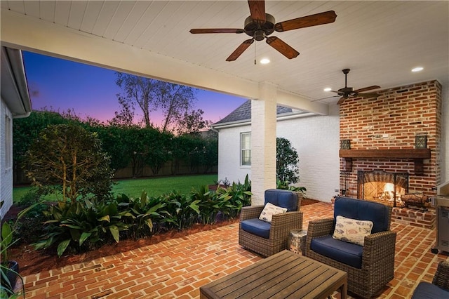 patio terrace at dusk featuring ceiling fan and an outdoor brick fireplace