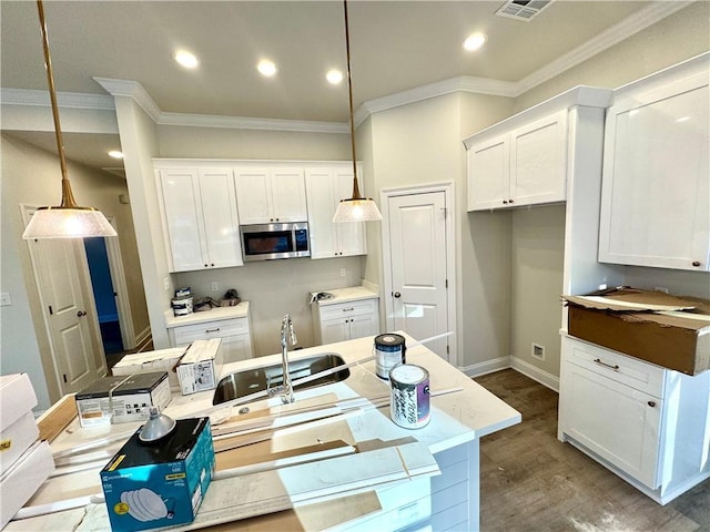 kitchen featuring white cabinetry, stainless steel microwave, crown molding, and wood finished floors