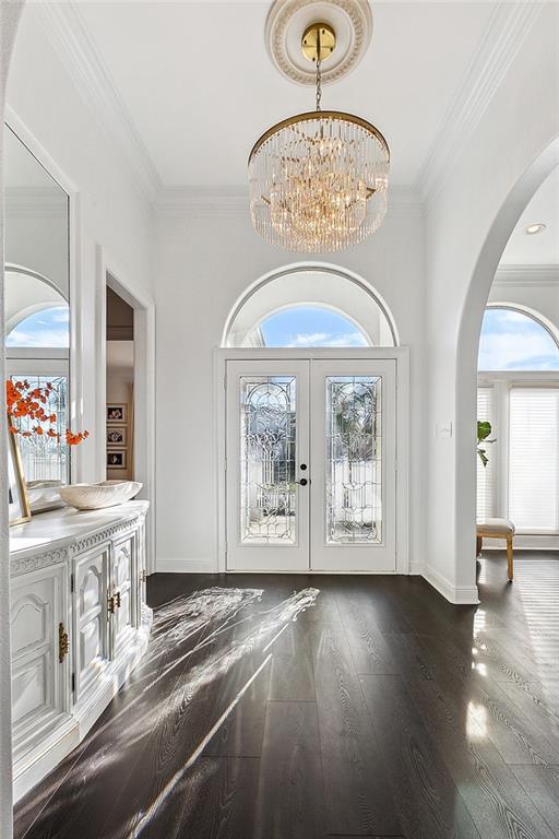 foyer entrance featuring a notable chandelier, ornamental molding, french doors, and dark hardwood / wood-style flooring