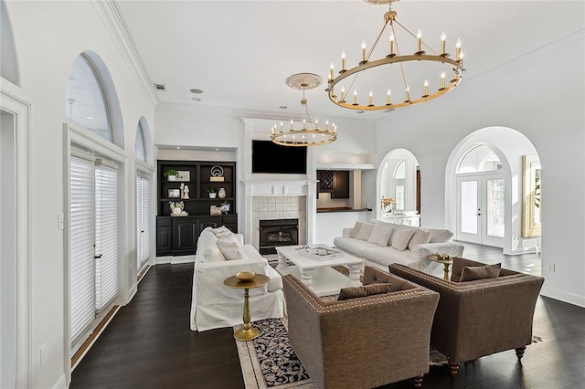 living room with french doors, dark wood-type flooring, a chandelier, a tile fireplace, and crown molding