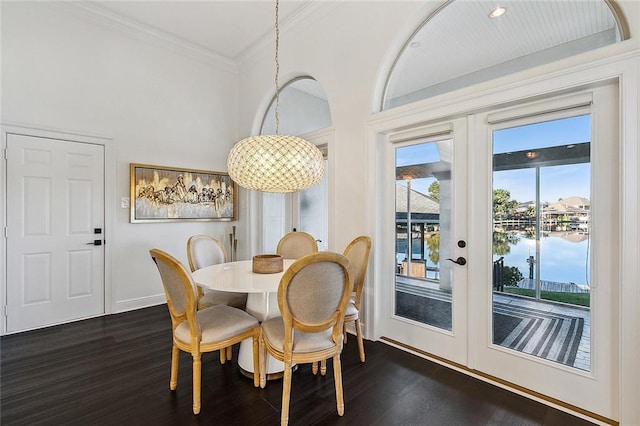 dining space with french doors, a water view, dark wood-type flooring, and crown molding