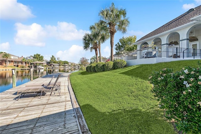 dock area with a lawn, a water view, and a balcony