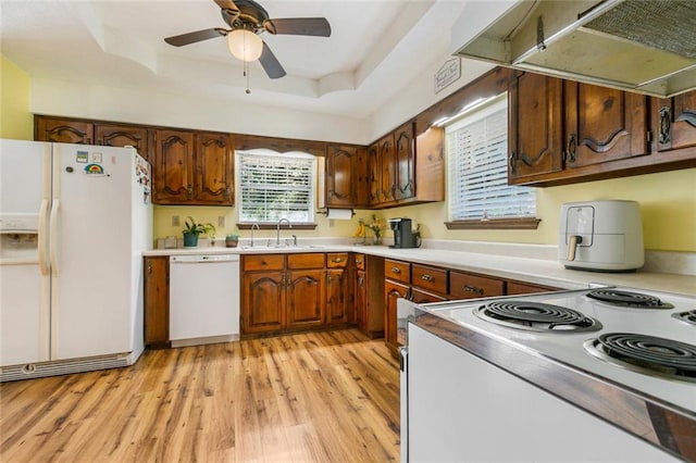 kitchen featuring white appliances, sink, light wood-type flooring, a tray ceiling, and range hood