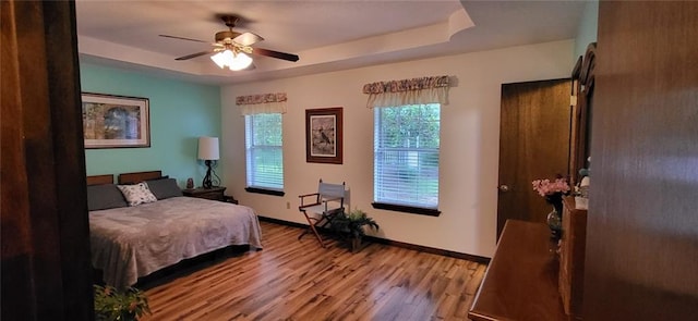 bedroom with light hardwood / wood-style flooring, a raised ceiling, and ceiling fan