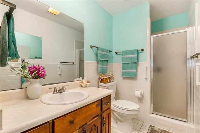 bathroom with a shower with door, tile patterned floors, toilet, vanity, and tile walls